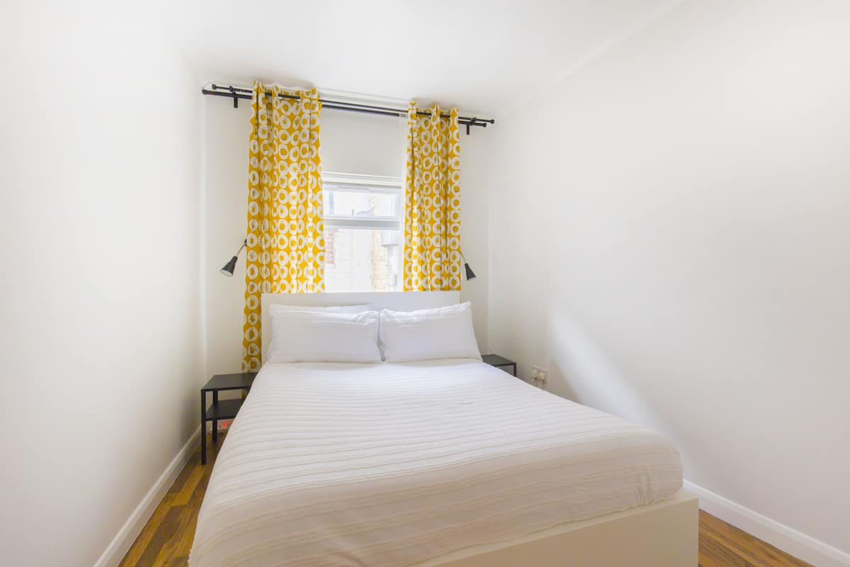 A bedroom with a bed, curtains, a nightstand, and a lamp.