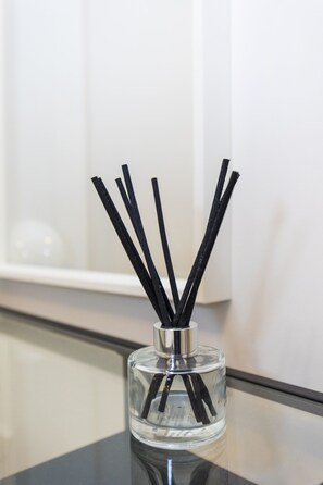 A clear glass bottle with black reed sticks on a reflective surface.