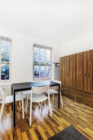 A room with a wooden floor, white chairs, a dark table, and a large wardrobe.