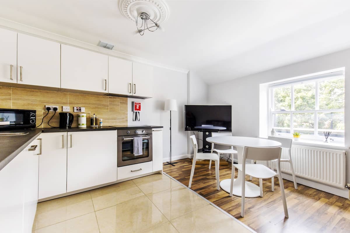 A modern kitchen with white cabinets, a built-in oven, a microwave, and a dining area with a round table and chairs.