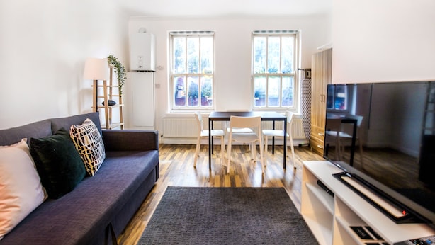 Una sala de estar moderna con un sofá, una mesa de comedor con sillas, un televisor y ventanas grandes.