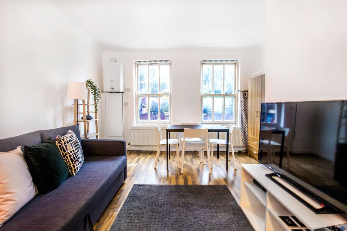 A modern living room with a sofa, a dining table with chairs, a TV, and large windows.