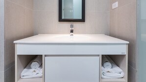 Ein modernes Badezimmer mit einem weißen Waschtisch, einem Spiegel und zwei Handtuchregalen.