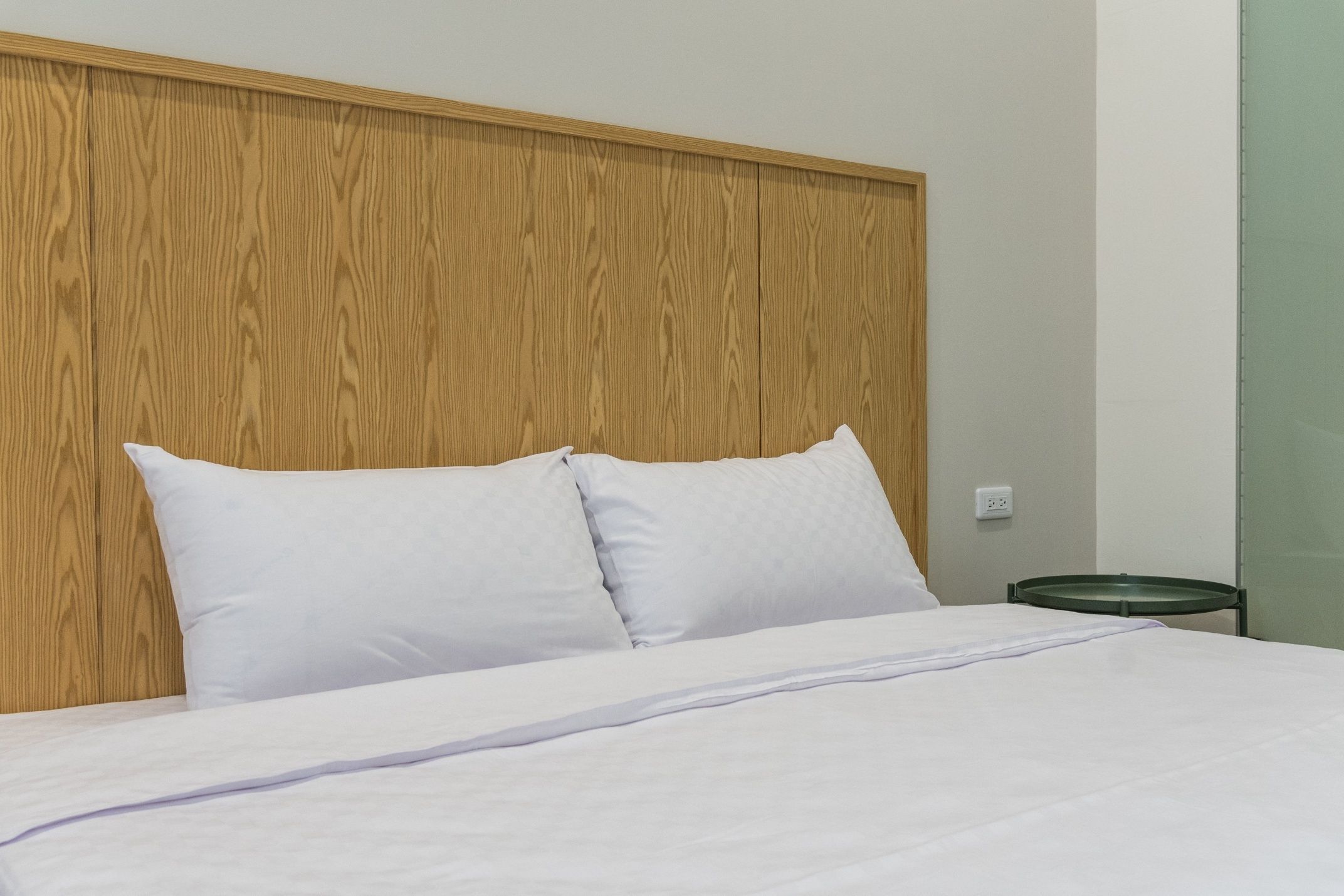 A neatly made bed with white linens and pillows, a wooden headboard, and a small bedside table with a green tray.
