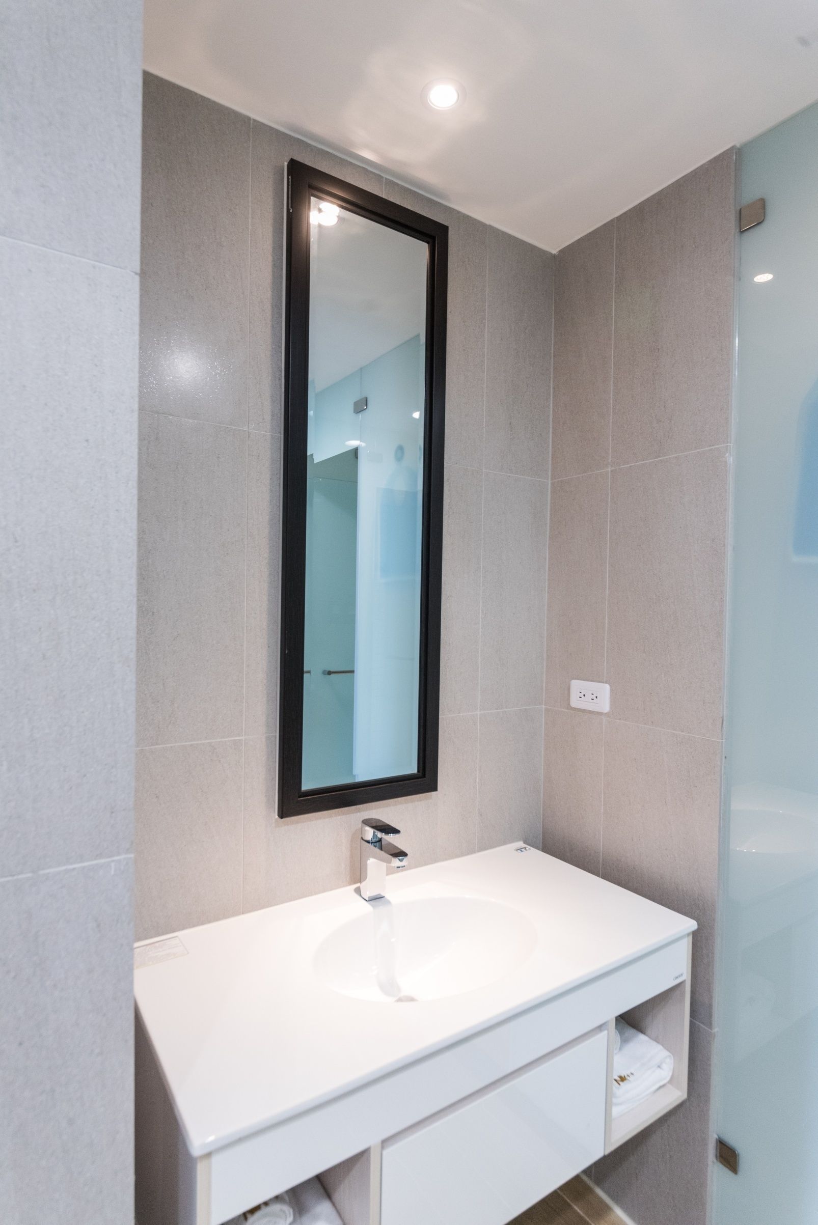 A modern bathroom with a white sink, a large mirror, and tiled walls.