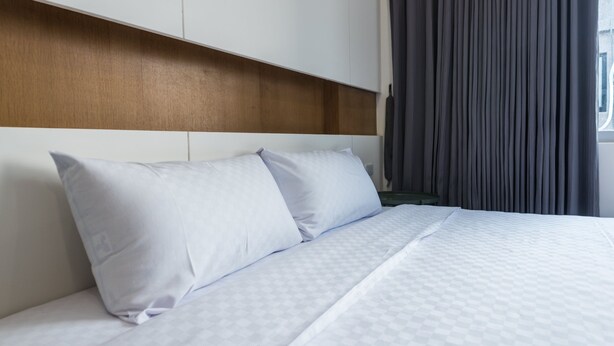Ein Hotelzimmer mit einem großen Bett, weißer Bettwäsche, einem Holzkopfende und einem dunklen Vorhang.