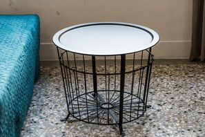 Una mesa redonda de metal con cubierta blanca, sobre un suelo de terrazo junto a una cama color turquesa.