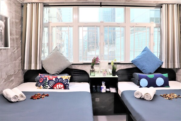 A hotel room with two beds, a small table with toiletries, and a window with curtains.