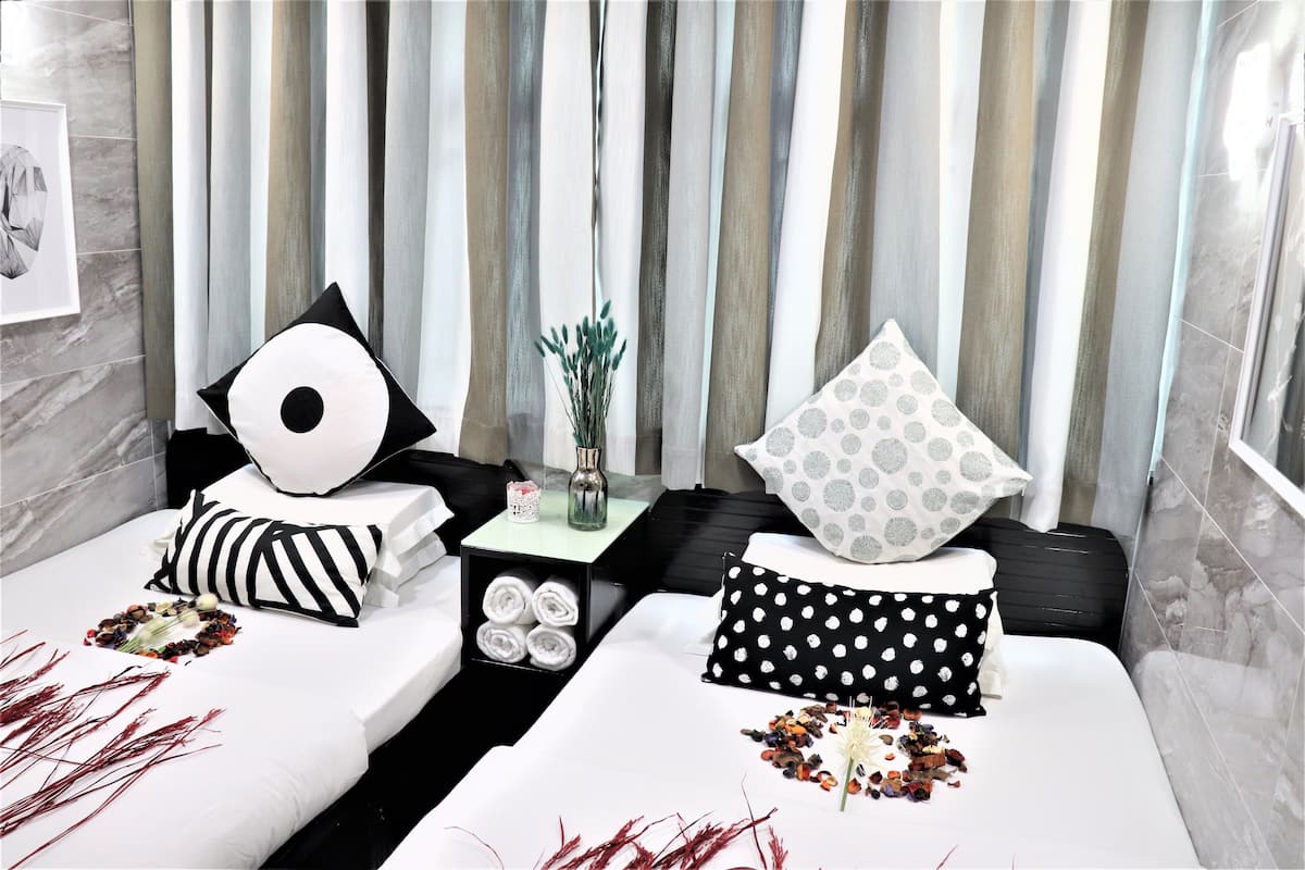 A modern hotel room with two beds, striped curtains, a vase with dried plants, and a framed picture on the wall.