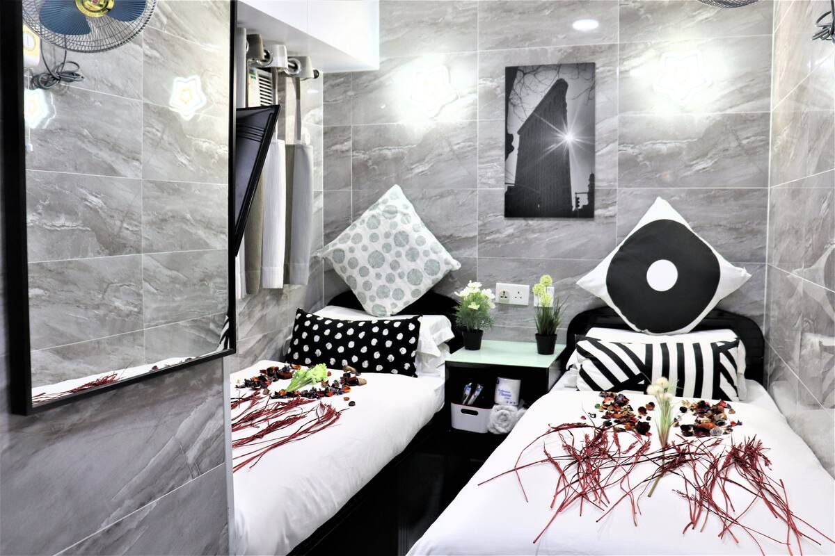 A modern hotel room with two beds, a large mirror, a wall-mounted fan, and a small table with a potted plant.
