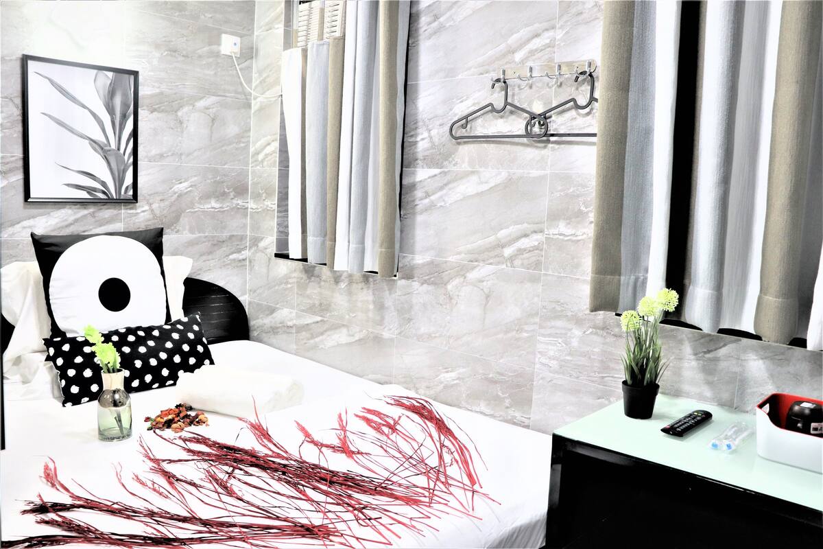 A modern hotel room with a marble wall, a bed with a polka dot pillow, a small plant, and a bedside table with a remote control and a bottle.
