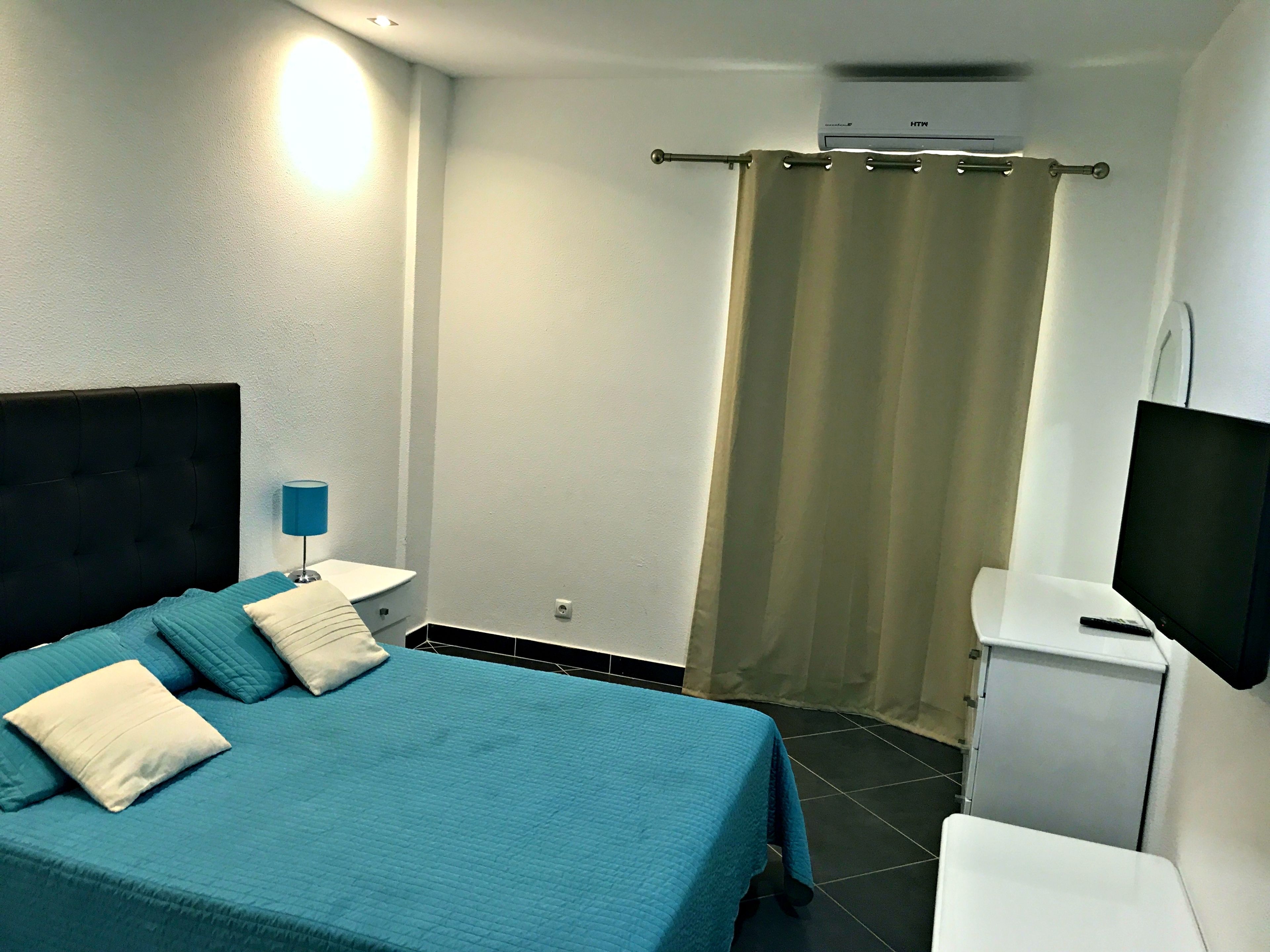 Una habitación de hotel con cama, televisión, escritorio pequeño y cortina.