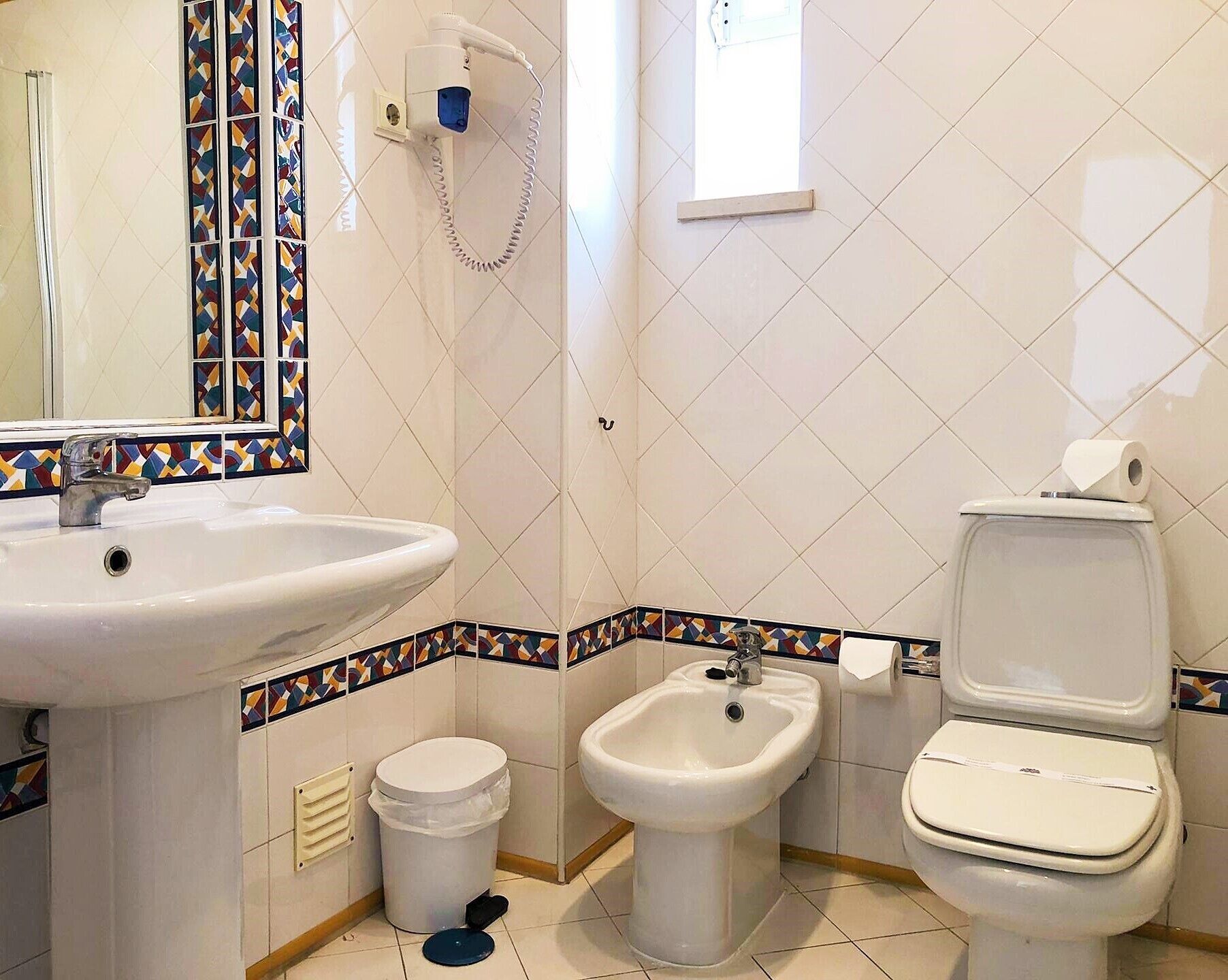 Un baño con lavamanos, bidé, inodoro y un cubo de basura.