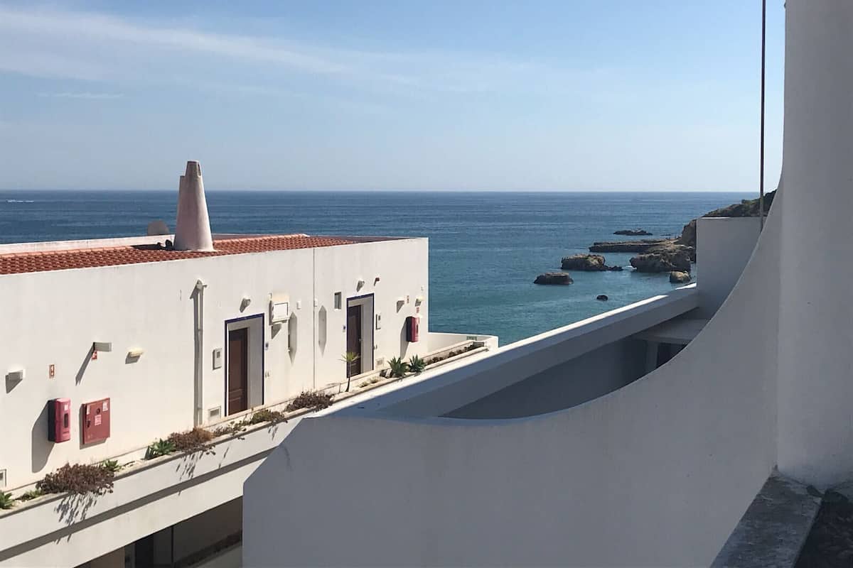 A modern building with a white facade, a red-tiled roof, and a view of the sea.