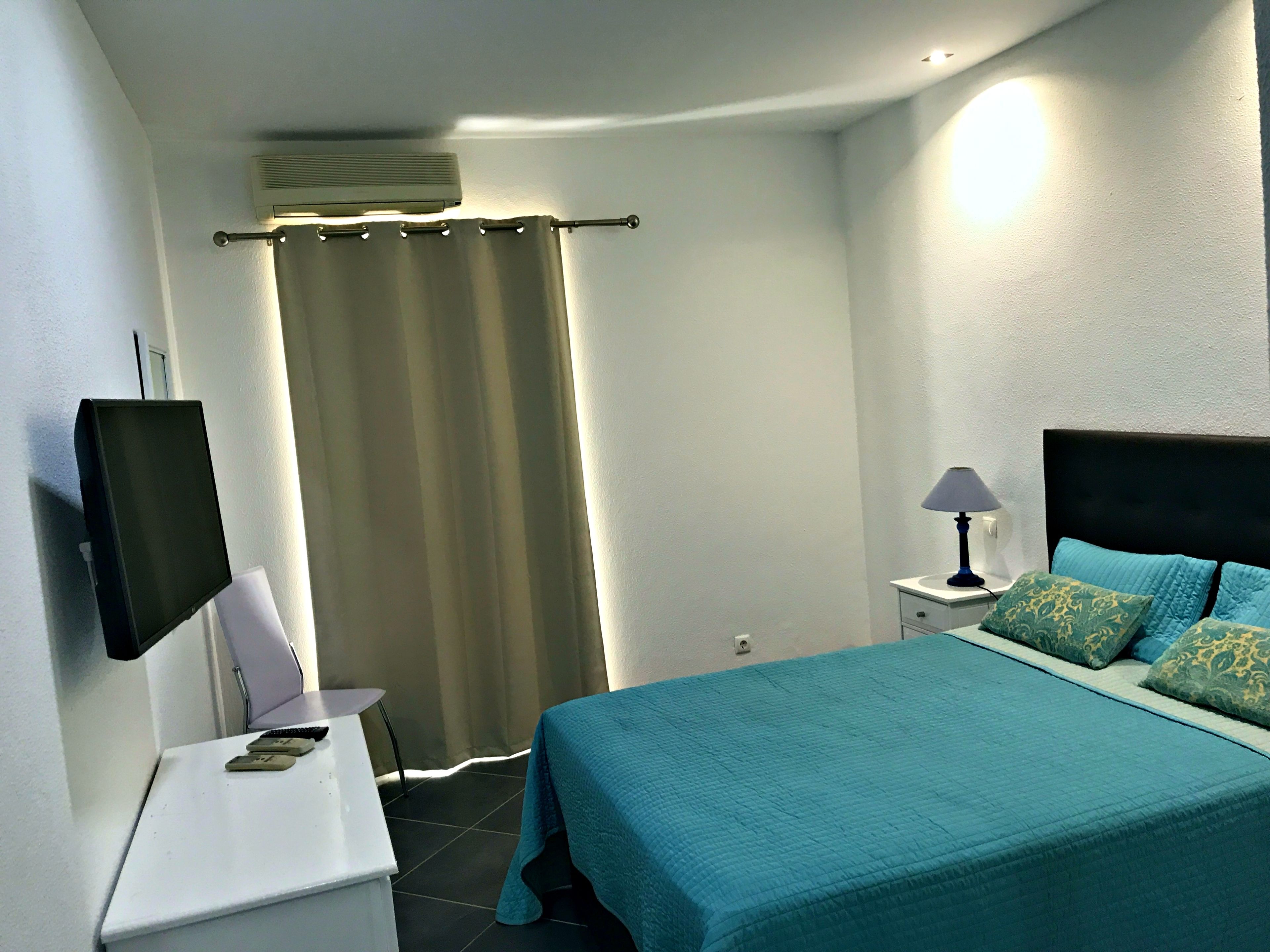 A bedroom with a bed, a TV, a desk, a lamp, and a curtain.