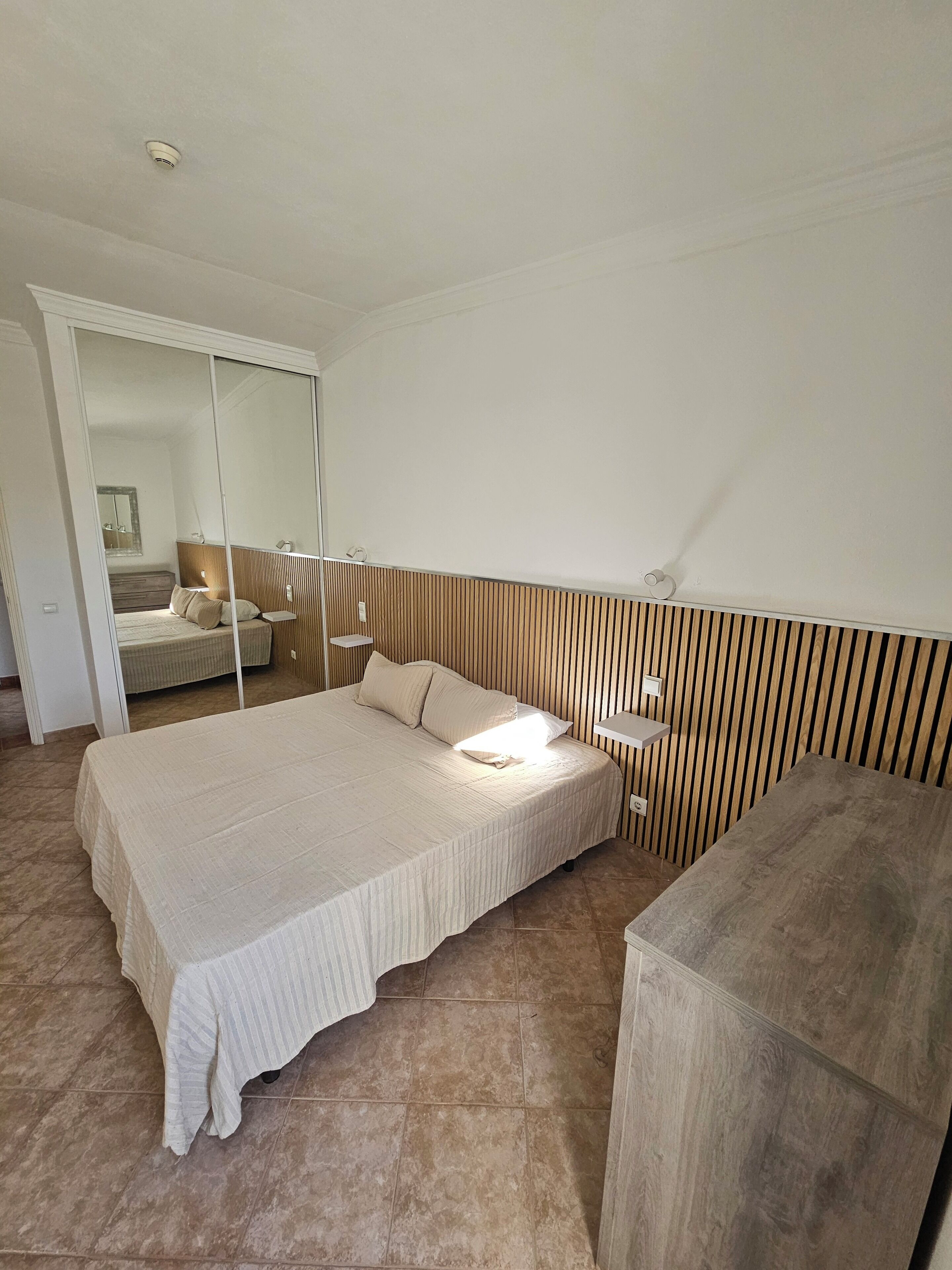 Ein Schlafzimmer mit einem großen Bett, einem Holzkopfende, einem Nachttisch und einem Spiegel.