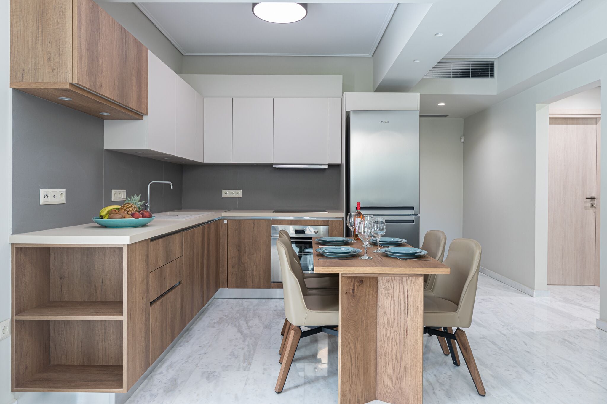 A modern kitchen with wooden cabinets, a built-in oven, and a dining area with a table and chairs.