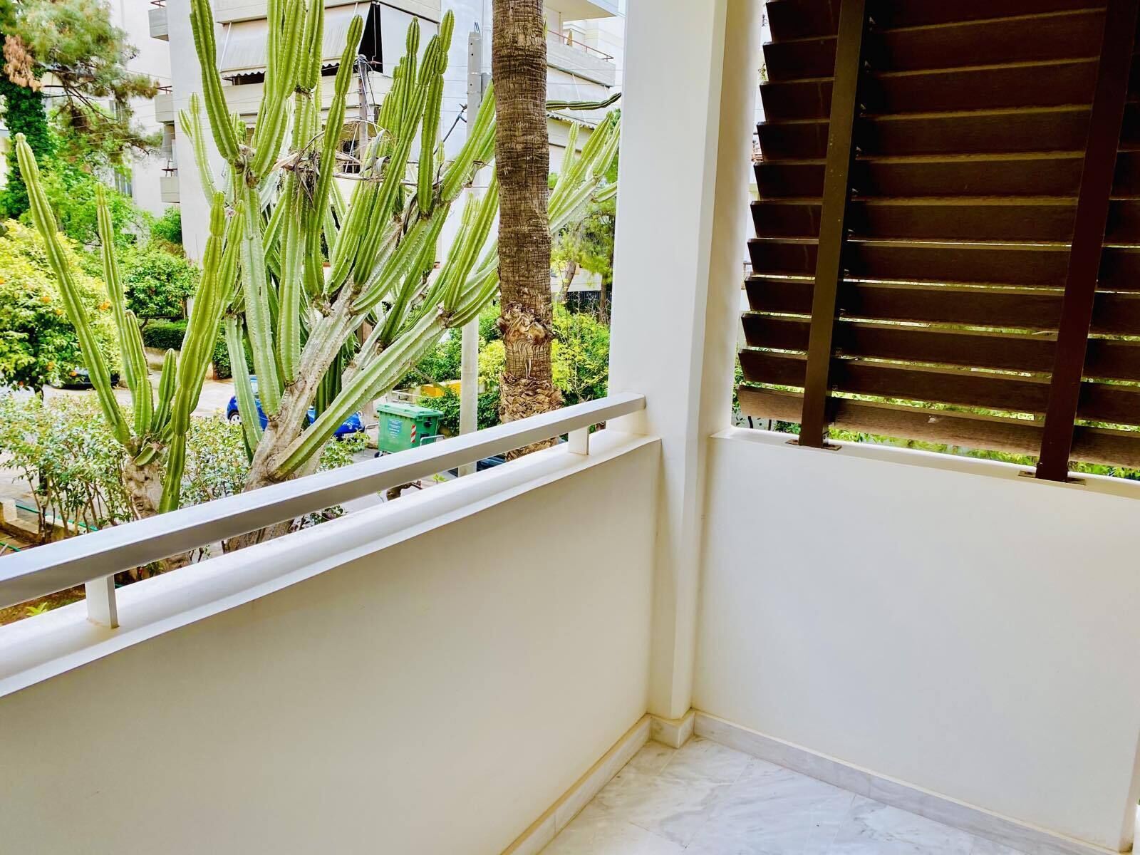 A balcony with a white railing, a view of a garden with cacti, and a building in the background.