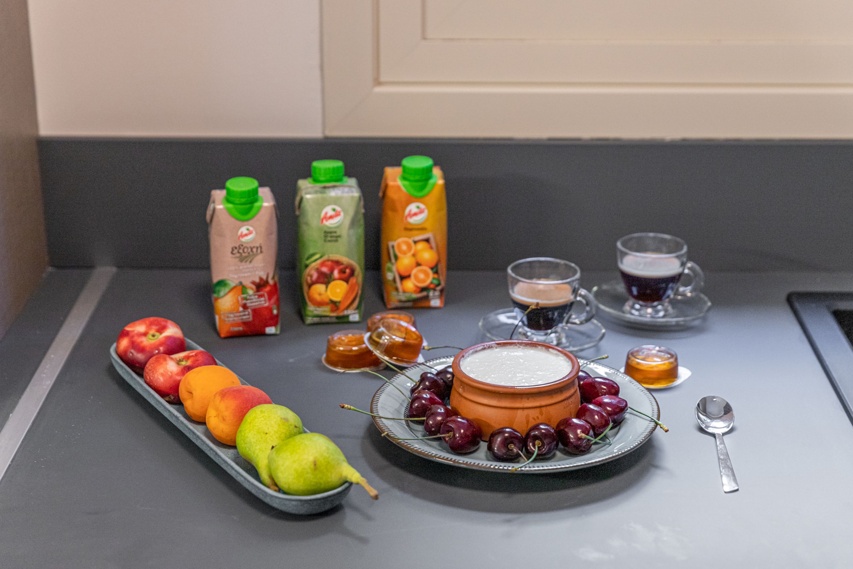 A breakfast setting with various fruits, juices, and a bowl of yogurt parfait on a table.