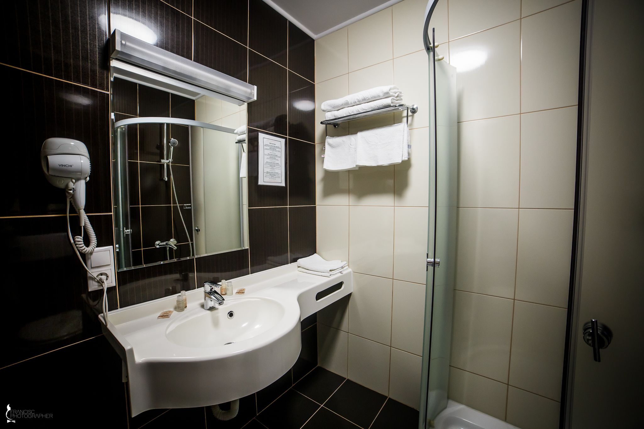 A modern bathroom with a white sink, a hairdryer, a glass shower enclosure, and a towel rack.