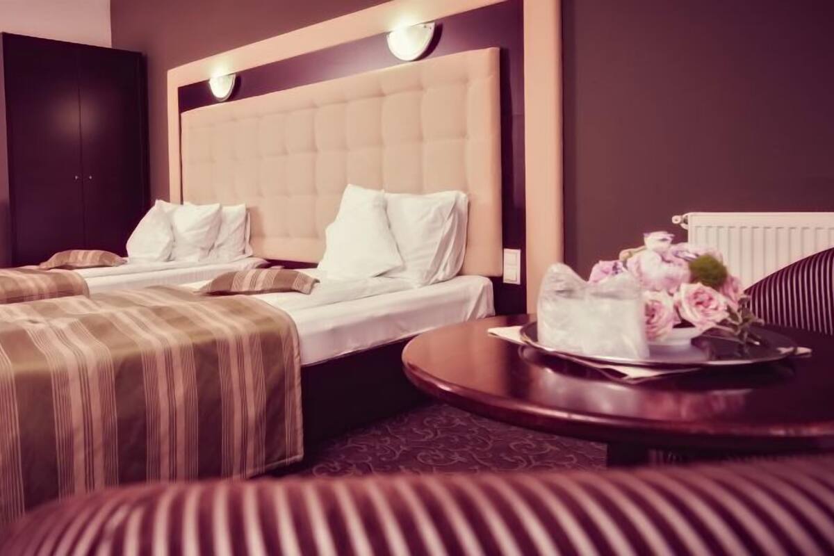 A hotel room with two beds, a large padded headboard, a round table with a tray of flowers, and a dark-colored wardrobe.