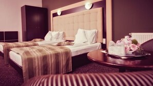 Een hotelkamer met twee bedden, een groot hoofdeinde, een klein tafeltje met een schaal bloemen en een donkere kast.