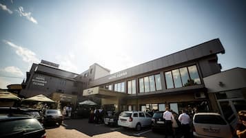 Un hotel con un letrero que dice "HOTEL OZANA" y "RESTAURANT OZANA". Hay coches estacionados al frente, y se ve gente caminando hacia la entrada.