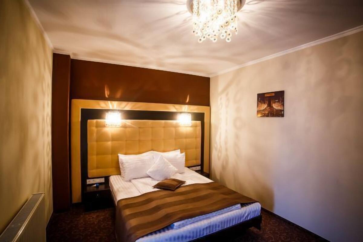 A hotel room with a large bed, a headboard with lights, a radiator, and a small picture on the wall.