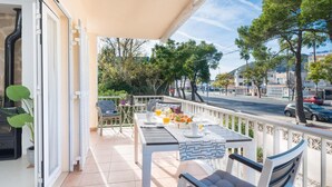 A balcony with a table set for breakfast, outdoor seating, and a view of the street and trees.