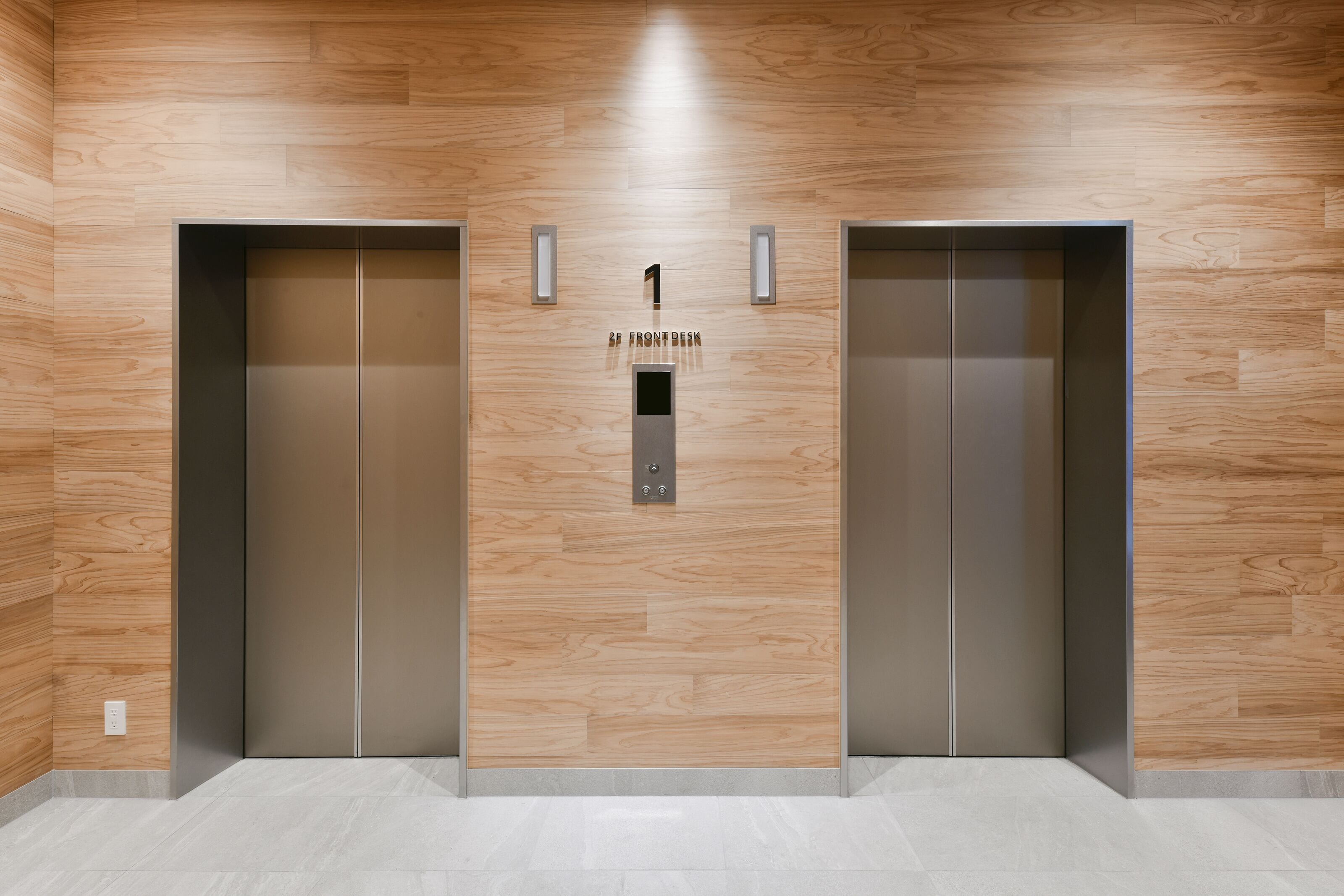 Two elevator doors with a wooden wall and a sign above them.