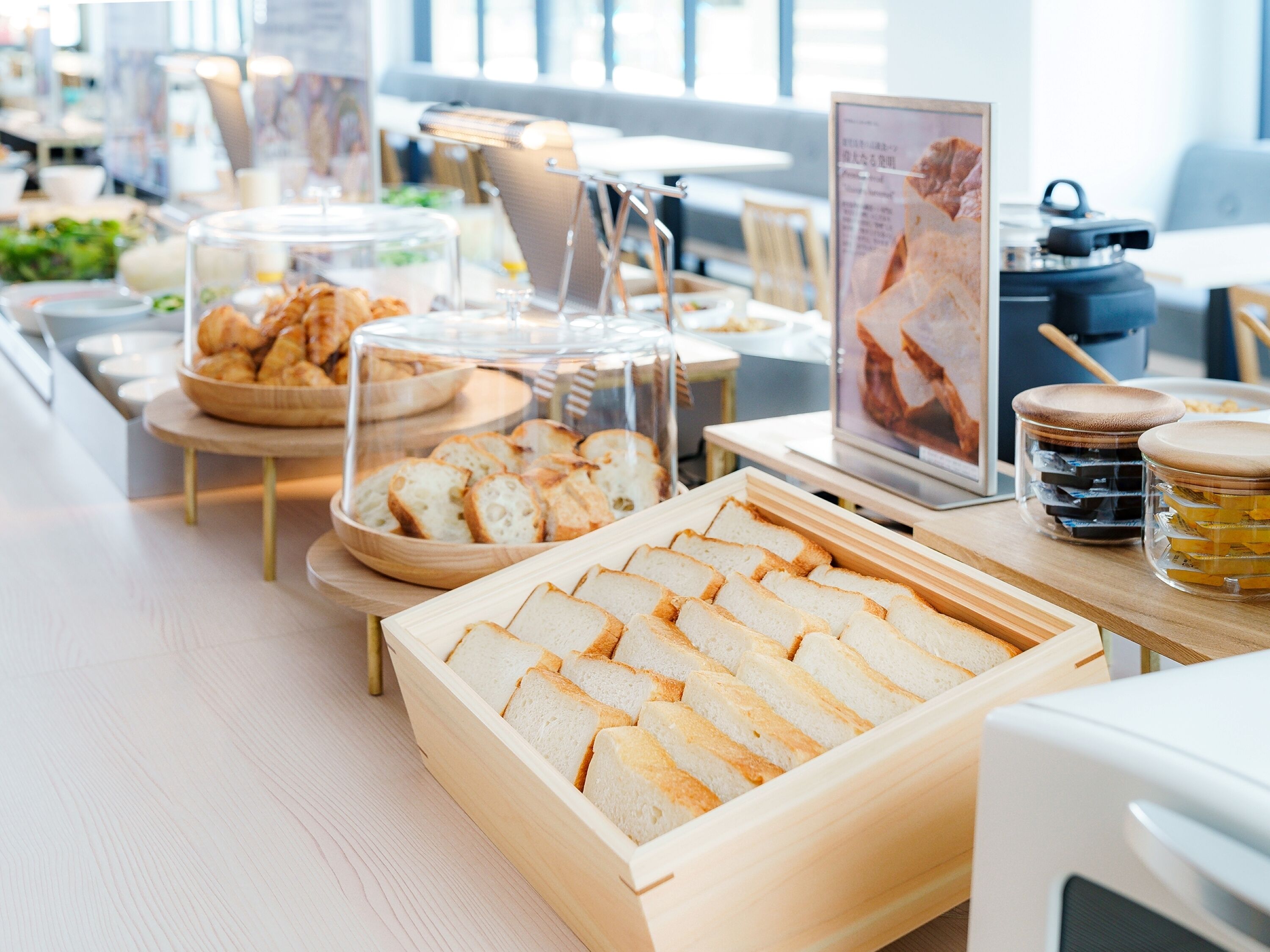 A buffet setup with bread, pastries, and jars of condiments.