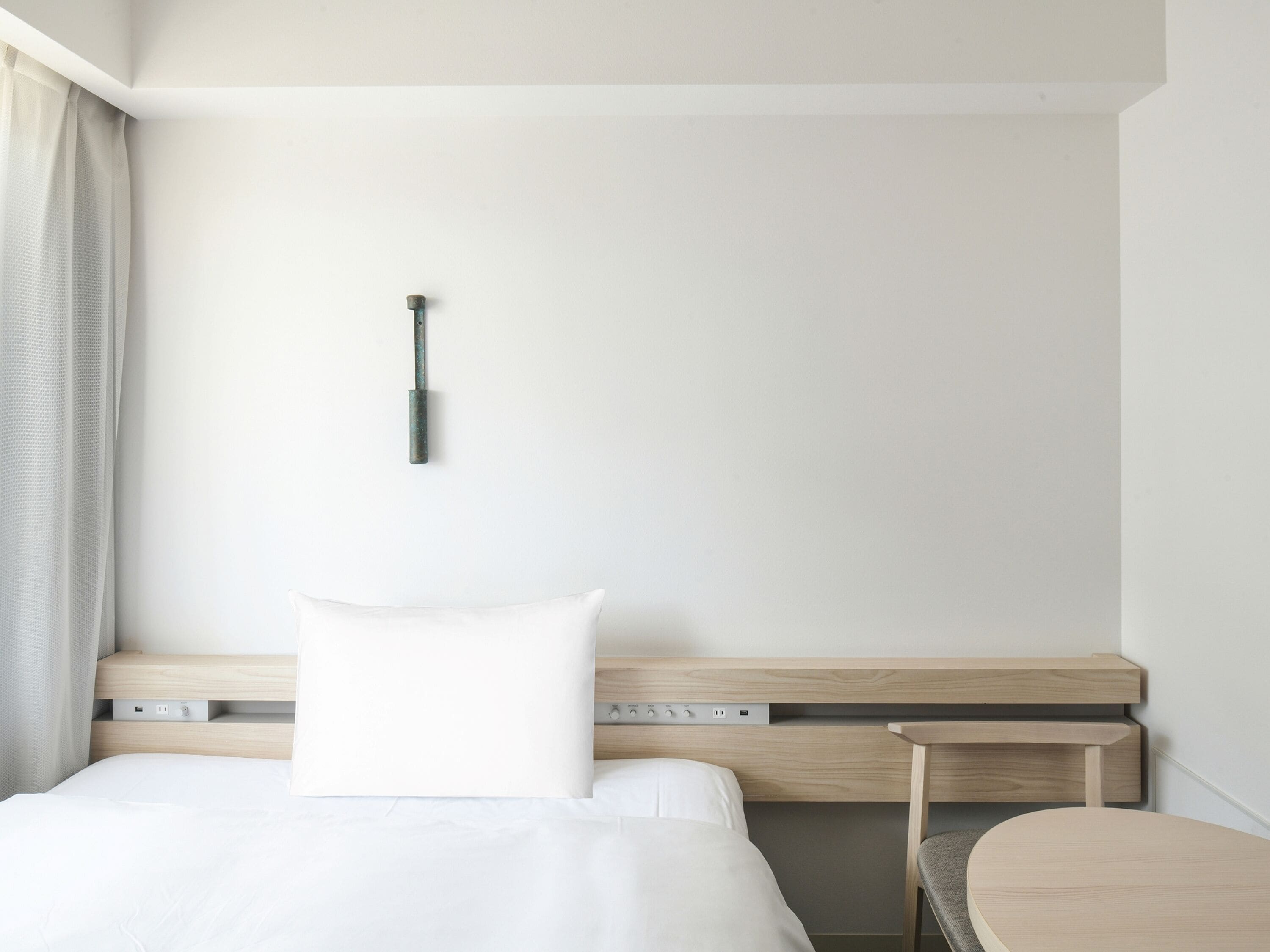 A modern hotel room with a bed, bedside tables, a desk, and a wall-mounted lamp.