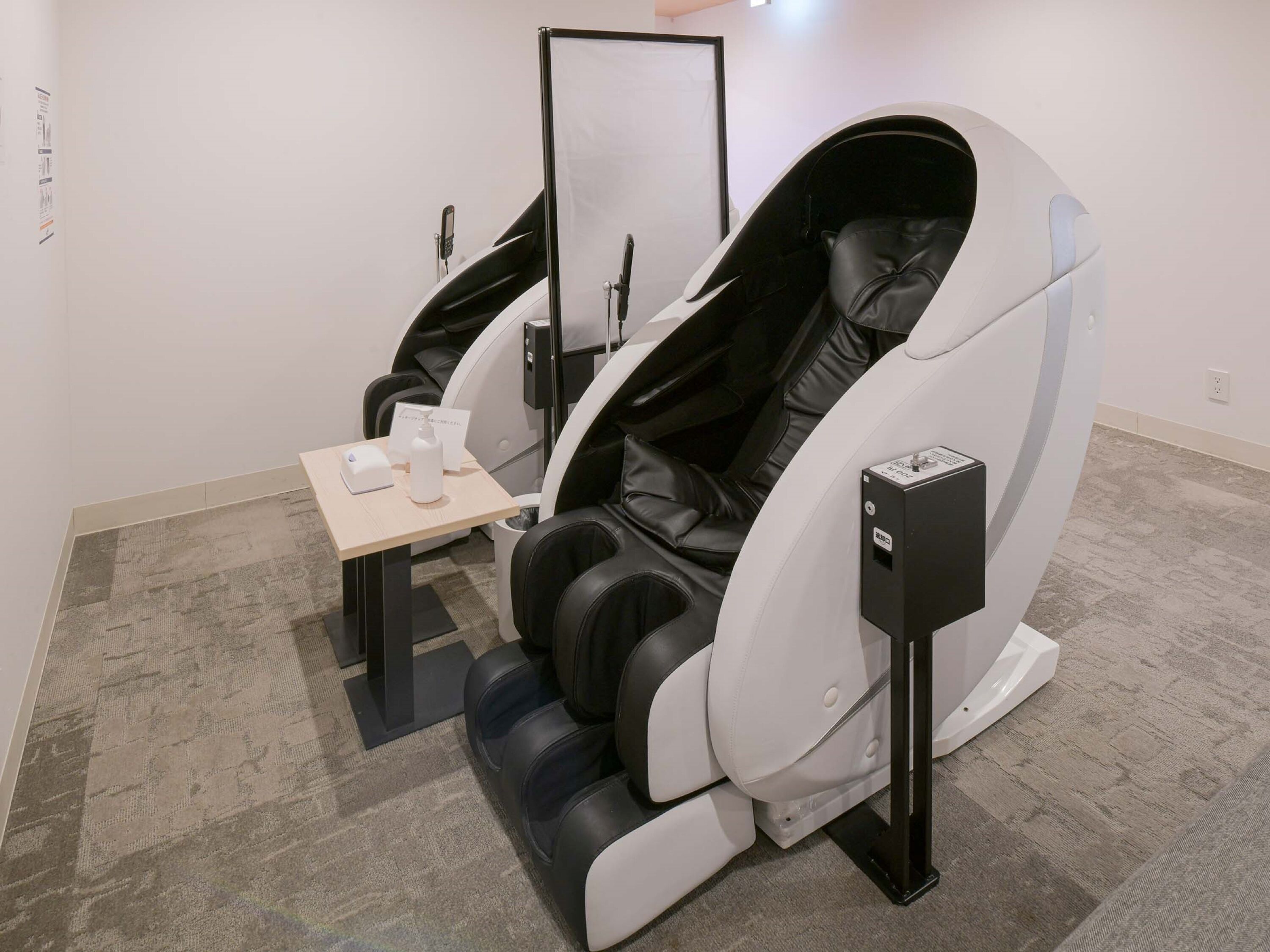 A modern massage therapy room with a reclining chair, a small table with a bottle and a cup, and a control panel.