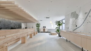 A spacious lobby with a wooden bench, a reception desk, a map on the wall, and potted plants.