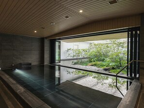Un espace piscine intérieur moderne, doté d’un mur en verre qui offre une vue sur un jardin.