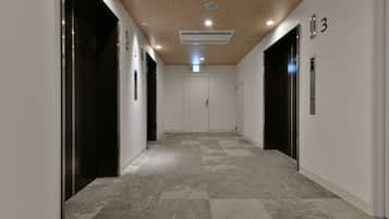A modern hallway with two elevators, a light-colored carpet, and a wooden ceiling.