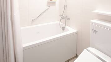 Ein modernes Badezimmer mit einer weißen Badewanne, einer Toilette und einer Duschkabine. Über der Badewanne befindet sich ein Ablagefach mit Pflegeprodukten.