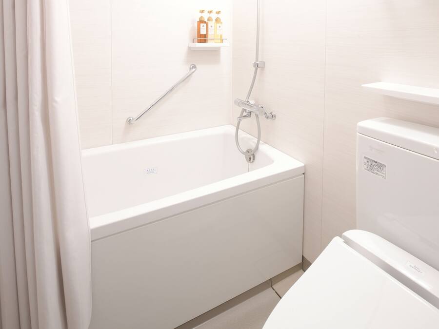 Ein modernes Badezimmer mit einer weißen Badewanne, einer Toilette und einer Duschkabine. Über der Badewanne befindet sich ein Ablagefach mit Pflegeprodukten.