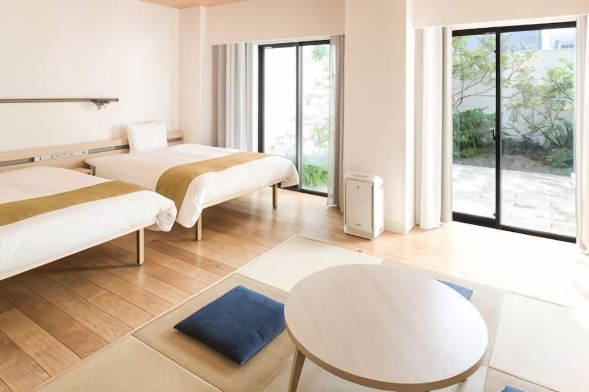 A hotel room with two beds, a round table, and a sliding glass door to the outside.