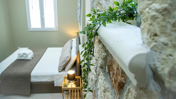 Ein Schlafzimmer mit einer Steinsturz, einem Bett mit weißer Matratze und brauner Decke, einem Nachttisch mit Lampe und einem Fenster mit Jalousien.