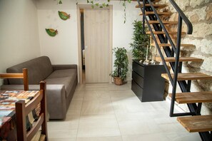 A living room with a sofa, a wooden table, a staircase, and potted plants.