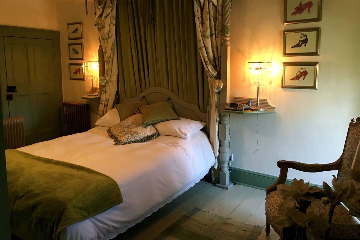 A bedroom with a four-poster bed, a nightstand with a lamp, and three framed pictures on the wall.