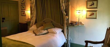 A bedroom with a four-poster bed, a nightstand with a lamp, and three framed pictures on the wall.