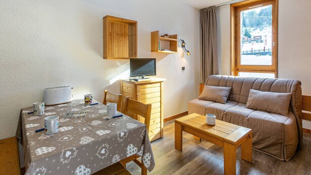 A cozy room with a wooden desk, a computer, a sofa, and a dining table with heart-patterned tablecloths.