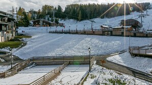 A snow-covered ski resort with buildings, a ski lift, and a clear sky.