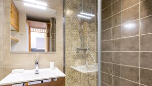 A modern bathroom with a glass-enclosed shower, a wooden vanity, and patterned tiles.