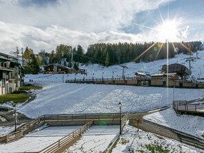 A snow-covered ski resort with buildings, a ski lift, and a clear sky.