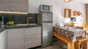 A compact kitchen with a refrigerator, microwave, and sink. There is a dining area with a table and benches.