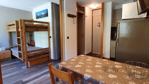 A compact room with a bunk bed, a dining table with a patterned tablecloth, a refrigerator, and a television.