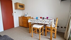 A small, compact room with a wooden table set for two, a microwave above the table, and a red door to the left. - Southwest cabin studio 4/6 pers near slopes in Chamrousse (Chamrousse)